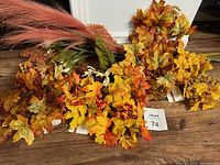 Photo showing multiple artificial flower stems laid out on wooden floor featuring autumn leaves and berries for a fall-themed arrangement.