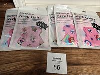 Five packs of Genovega neck gaiters in sealed plastic packaging showing colorful cartoon and heart designs inside each pack.