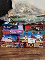 Stack of puzzle boxes including some in shrink wrap plus bags of loose puzzle pieces.