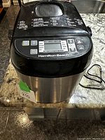 Front and top view of Hamilton Beach bread maker with power cord visible, placed on a kitchen countertop.