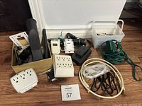 Overall view of household items including screws, timers, extension cords, power strips, and electrical parts arranged on floor with lot identifier card.