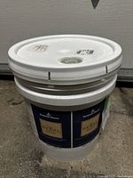 Large white plastic pail with lid containing Benjamin Moore Regal Select paint. Label visible showing brand and product details.