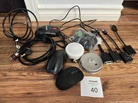 Lot showing all items including two black wireless mice, locking cable with keys, multiple computer cables, and two round LED puck lights on hardwood floor.