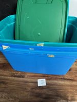 Photo showing blue plastic storage containers stacked with green lids inside, visible scratches and tape residue on exterior.