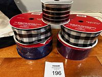 Lot of five spools of ribbon with various patterns and colors such as black and white checkered, glittery blue and purple, and sheer black with silver stripes.