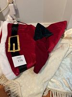 Photo of two Christmas tree skirts, one red velvet with white faux fur and black belt with gold buckle, and a cream-colored skirt with fringe edge.