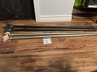 Two curtain rods, one black and one silver, placed side by side on the floor.