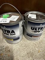 Two cans of Benjamin Moore Ultra Spec 500 paint placed on a concrete surface under wooden background, clearly showing brand and series labels.