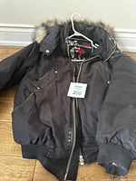 Full view of Moose Knuckle black men's jacket with fur-trimmed hood, showing front, zipper, and fabric condition.