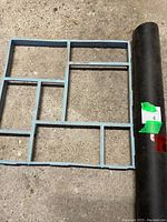 Partial roll of tar paper and blue plastic QUIKRETE Walk Maker stencil laid flat on concrete ground.