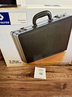 Black Samsonite business case briefcase in front of original box showing brand, warranty, and front exterior of the case.