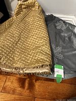 Two Christmas tree skirts folded on floor, one gold quilted with beaded fringe, one silver with snowflake embroidery.