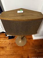 Front view showing the full speaker with wood grain cabinet and tulip stand on hardwood floor.