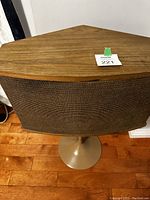 Front angled view showing wooden cabinet and woven grille cloth on speaker mounted on black pedestal tulip stand.