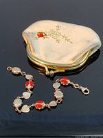 Sterling silver ladybug link bracelet alongside white leather change purse showing ladybug decoration and gold floral details.