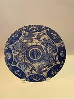 Full view of round antique blue and white Chinese porcelain plate with floral and bird design, visible chip on edge.