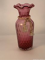 Front view of antique cranberry glass vase with ruffled top and cream silk cord tied around neck.