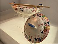 Side view of tureen showing floral pattern, double blue handles, and wooden utensil resting on top