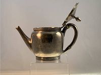 Side view of the antique silver teapot showing rounded body, spout, and heat resistant spacers on the handle.