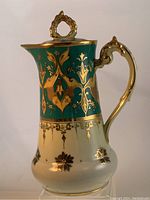 Full side view of the antique Viennese porcelain chocolate pot showing detailed gold designs on green and cream background.