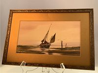 Full view of framed watercolour painting showing small sailboat grounded in bay, with beige mat and ornate frame, glass missing