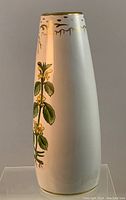 Full view of the white ceramic vase with hand painted botanical elements along the side and gold detailing near the opening