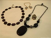 Full view of the four costume jewelry pieces arranged: purple faceted link necklace, adjustable pendant necklace, dancer head ring on chain, and earrings.