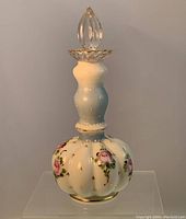 Full view of the antique milk glass perfume bottle with floral and gold gilt decoration and clear stopper.
