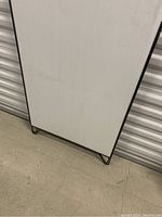 Front view of the metal framed sandwich board with white display surface, laid flat and showing some light wear marks