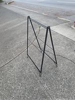 Front angle photo of empty black metal folding sandwich board sign showing its A-frame construction and crossbars for support.