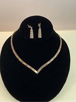 Full view of necklace and matching earrings displayed on black stand showing V-shaped mesh chain necklace and rectangular earrings.