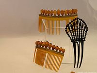 Pair of large Victorian gold-mounted hair combs topped with faceted amber beads, displayed alongside a smaller black celluloid comb with jet bead decoration.