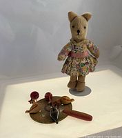 Photo of vintage mohair teddy bear in floral dress standing behind wooden hen mobile toy on white background.