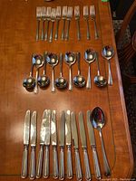 Full set of flatware on wooden table showing 8 forks, 9 spoons, 8 knives, and 1 serving spoon arranged in rows.