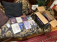 Lot of 10 books on a patterned sofa with one partially visible open box containing more books or items
