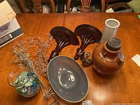 Full view of all items including the stoneware jug, wooden sconces, gray ceramic vase, decorative ceramic duck, glass bead branches, marbles in a glass bowl, and the serving bowl.