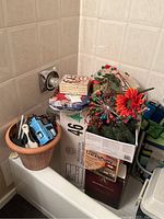 Box with assorted Christmas decorations including greenery, pine cones, ornaments and floral picks in a terracotta pot and other containers.
