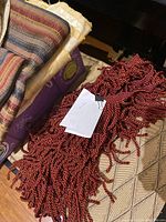 Close-up of a fringed red and black twisted rope-like fabric with a tag attached.