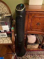 Full view of the black QuietSet tower fan about 40 inches tall placed next to furniture and boxes.