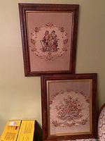 Both tapestries hung on a wall, upper one depicting classical figures and lower one a floral arrangement, framed in dark wooden frames.