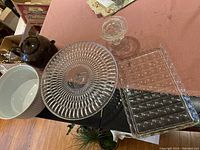 Photo showing clear glass cake plate, candle holder, two glass trays, brown Betty teapot, and white ceramic casserole dish on a pink cloth.