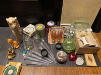 Overview of lot contents showing glass ball, pipettes, light bulbs, statues, coasters, and other small items