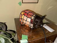 Pig shaped stained glass lamp on wooden table, side view showing lamp cord and color details.