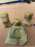 View showing two onyx bookends, faceted cube and square ashtray on a cloth surface with walking poles blurred in background.