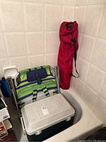 Photo showing two foldable outdoor camping chairs and a light gray Coleman cooler packed together in a corner indoors.