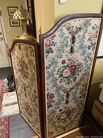 Two-panel folding privacy screen standing in a room, showing floral fabric and wood frame on both sides