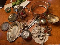 Photo showing silver-plated jug, trays, toast racks, serving ladle, and napkin rings arranged on table.