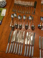 Overview of the flatware set showing arrangement of forks, dessert spoons, and large knives with polished silver plate finish.