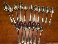 Full set of 18 silver plate spoons arranged on a wooden surface showing different sizes and wear.