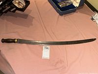 Full view of vintage curved sword with wood handle and brass collar on pink cloth.